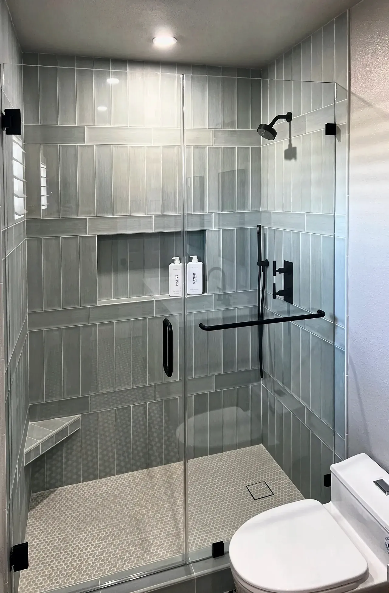 Shower tile with horizontal banding, a full-width niche, a corner bench and a penny-round pan