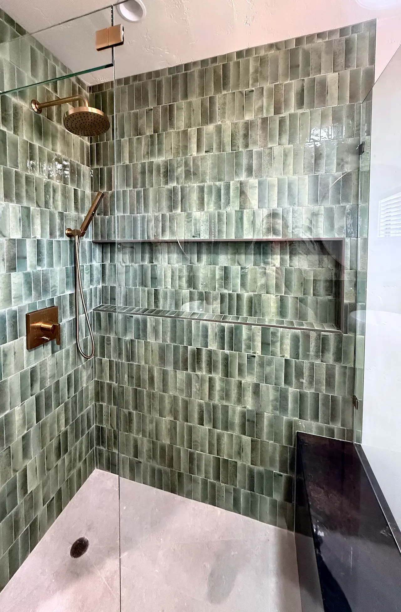 Green tile shower with brass fixtures and a built-in bench