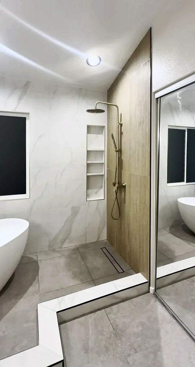 Walk-in shower with a wood-look tile wall, a brushed gold rain head and hand shower, a tall niche and a linear drain