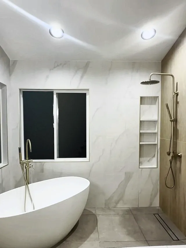 The same bathroom after the remodel, with a freestanding tub and an open walk-in shower in marble-look tile, a tall niche and a linear drain