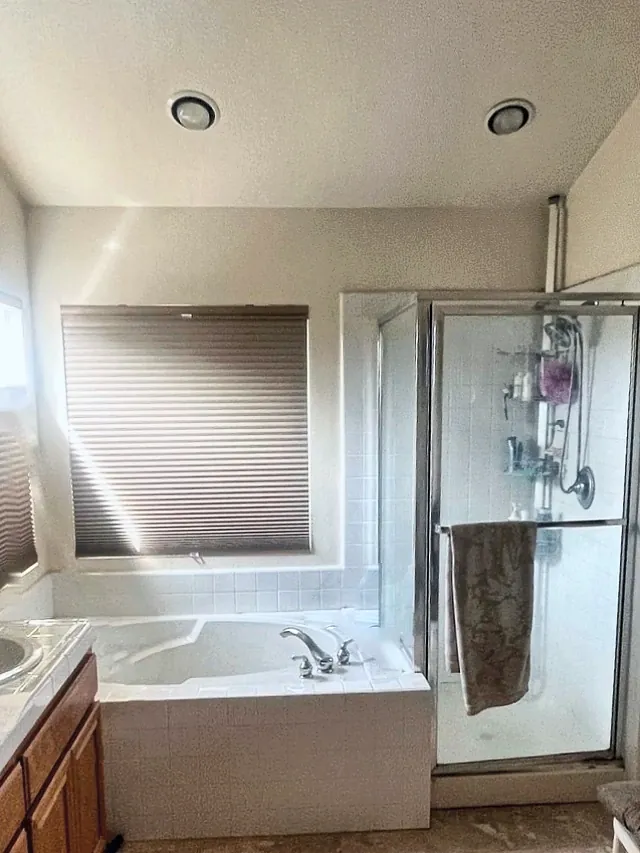 Rancho Peñasquitos primary bathroom before the remodel, with a drop-in tub in a white tile deck under the window and a framed glass shower stall