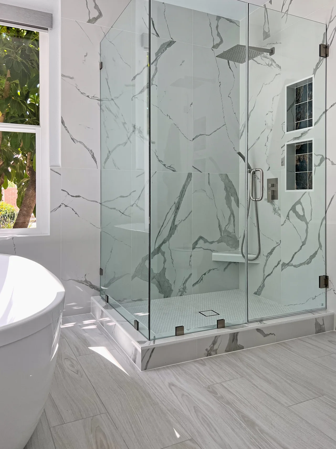 Frameless glass shower in marble-look tile with a bench and two niches