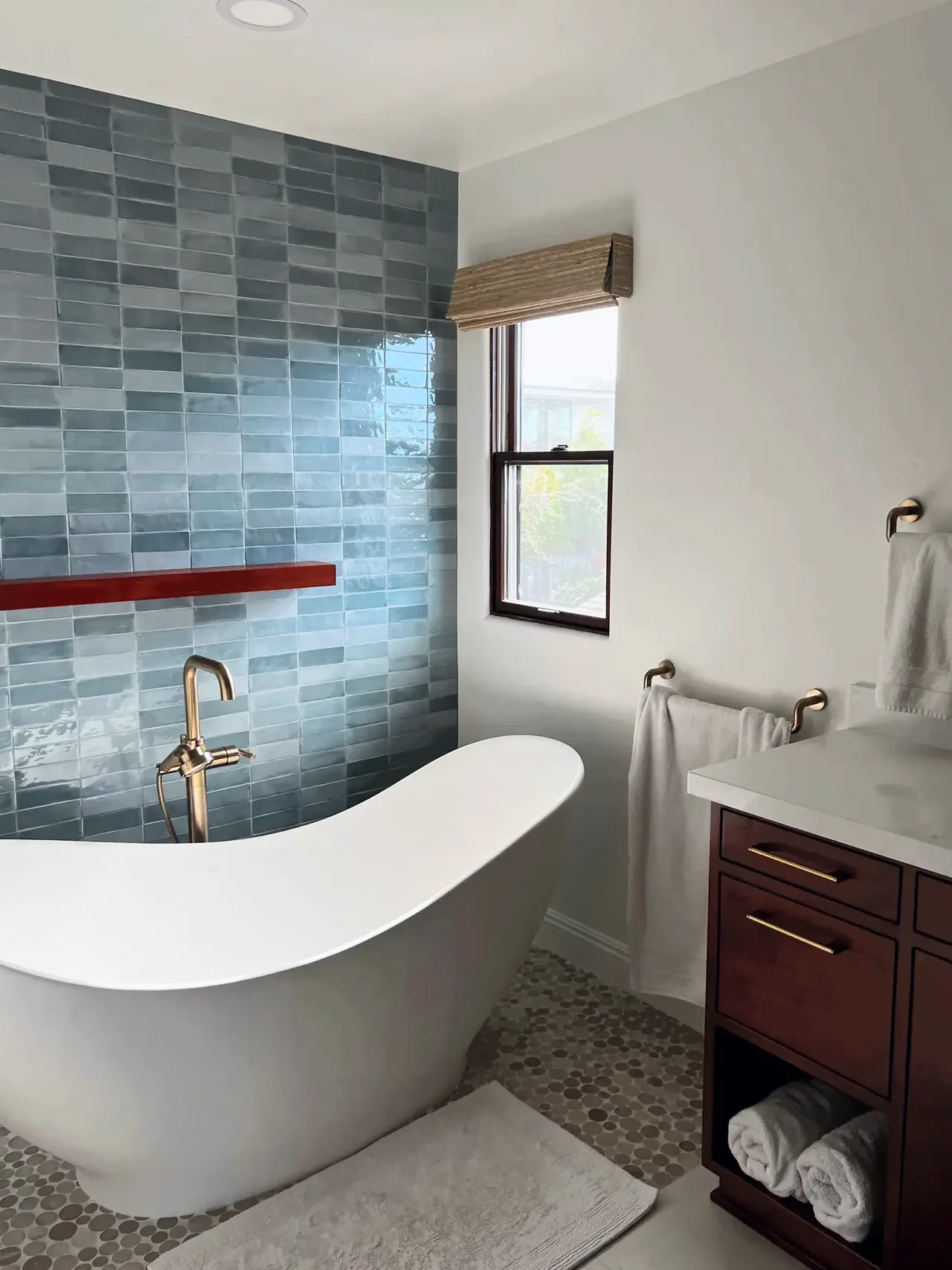 The same Del Mar bathroom after the remodel, with a freestanding slipper tub in front of a blue tile wall and a pebble mosaic floor