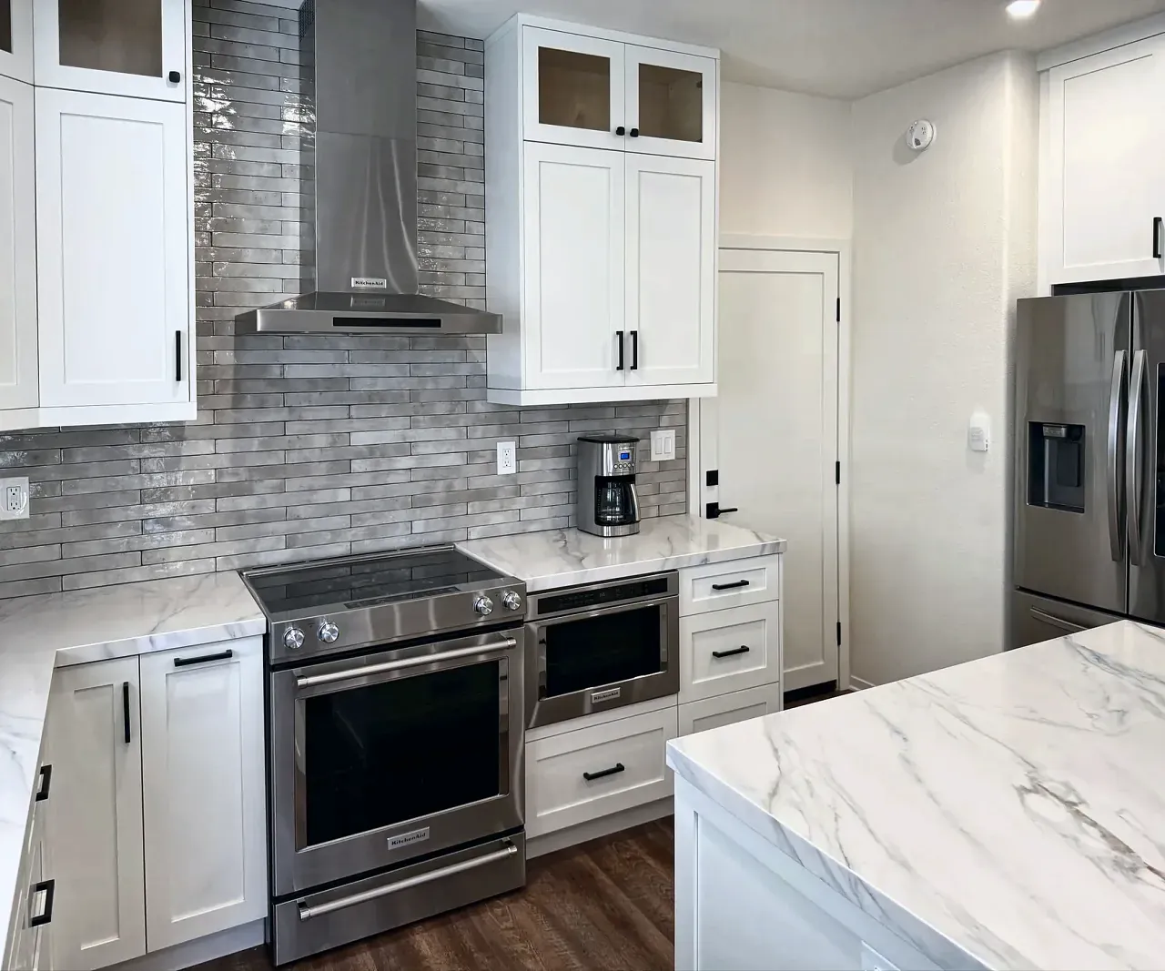 White shaker kitchen with a slide-in range, chimney hood and gray glossy tile backsplash
