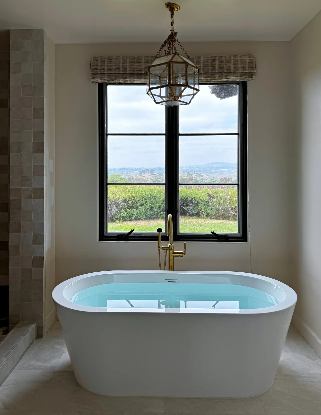 Freestanding tub under a black-framed window with a valley view, with a brass lantern above