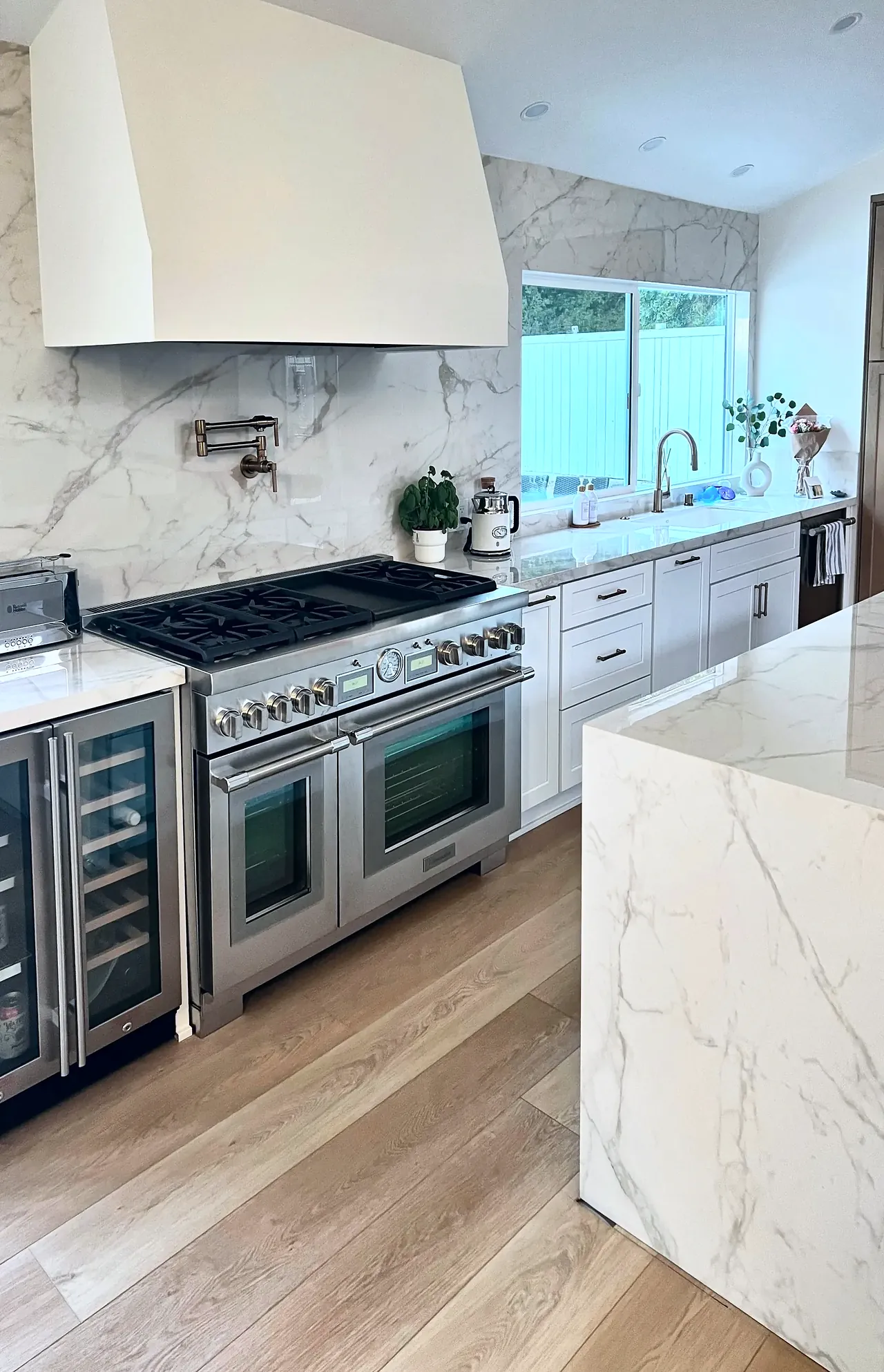 Pro-style range and wine fridge under a plaster hood with a slab backsplash