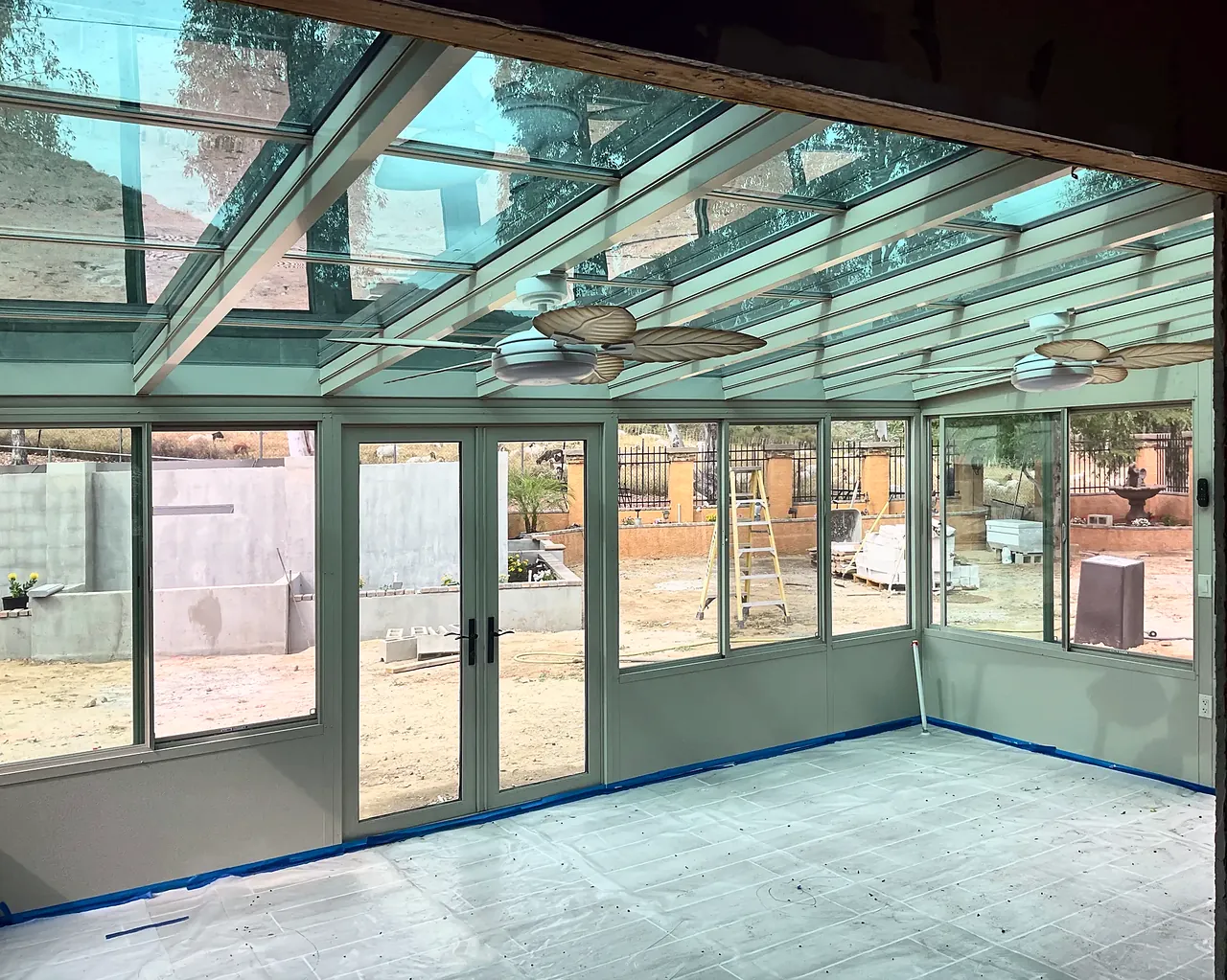 Inside the Fallbrook sunroom under the glass roof, with two ceiling fans and protective paper still on the floor