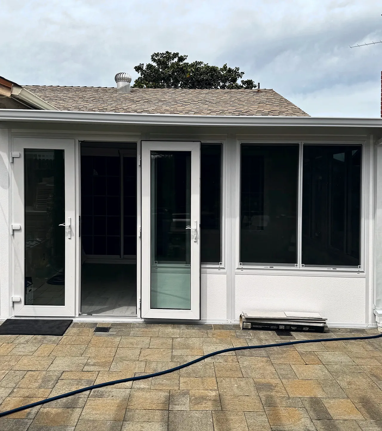The finished Four Seasons sunroom from the back patio, with glass French doors, sliding windows over a low solid wall and a solid white roof tucked under the house eave