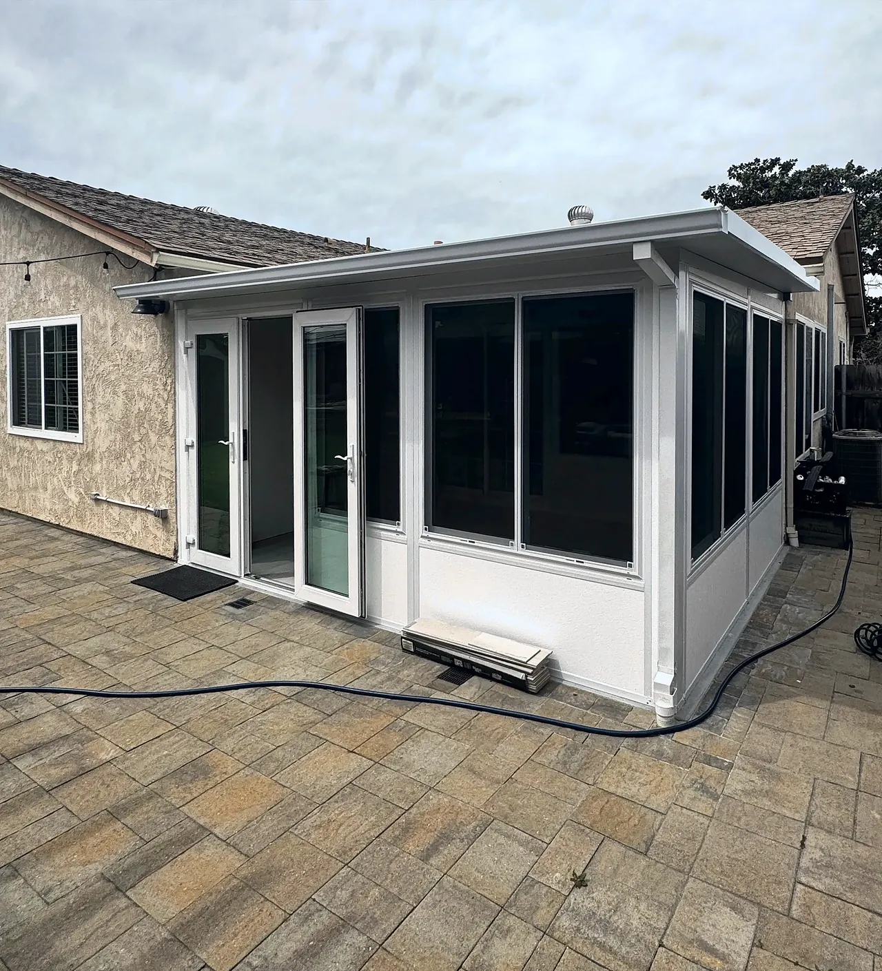The finished sunroom seen from the corner of the patio, filling the inside corner at the back of the house, with windows running along the side yard