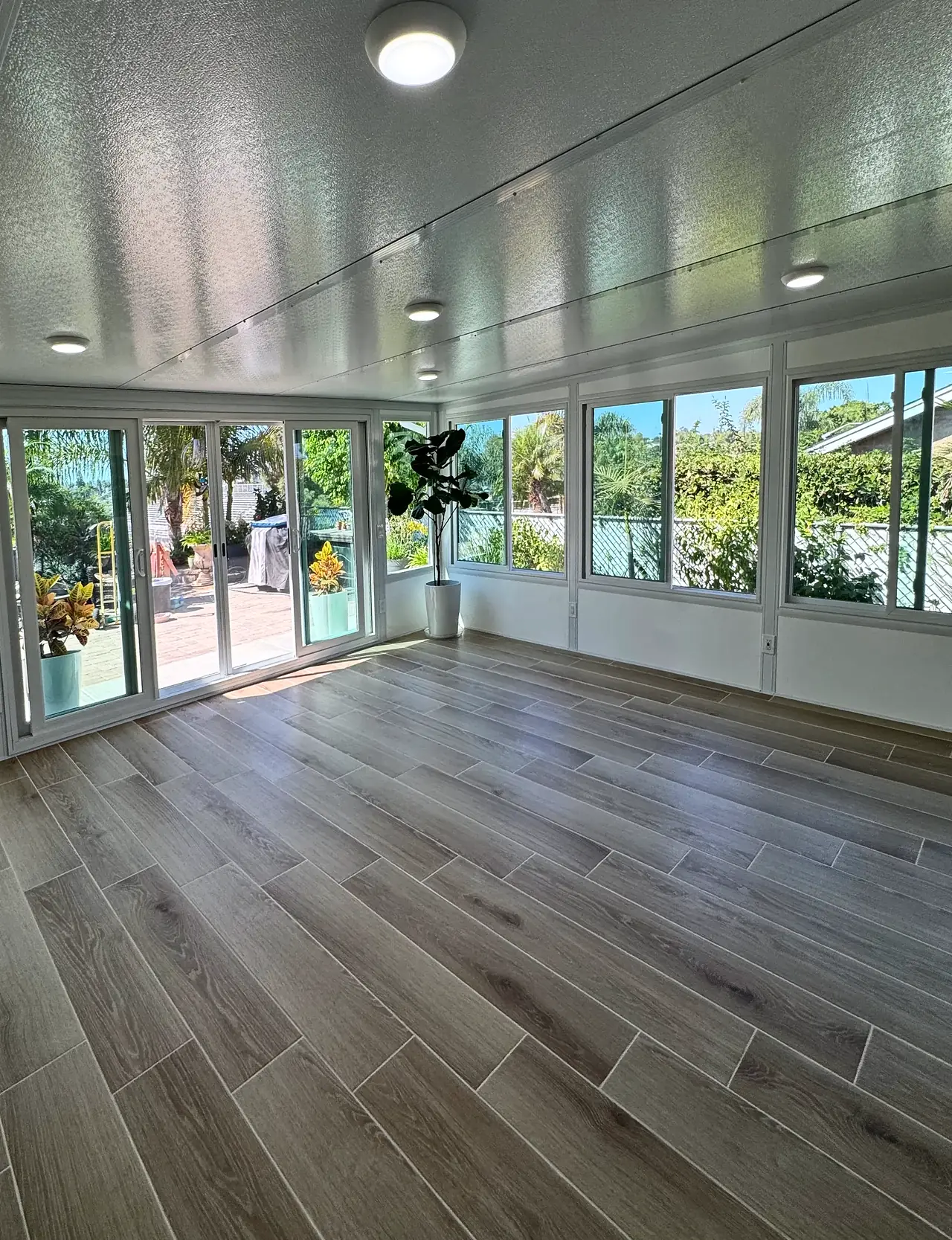 Inside the Vista sunroom, with ceiling lights, a four-panel sliding glass door and windows on two sides over a low white wall