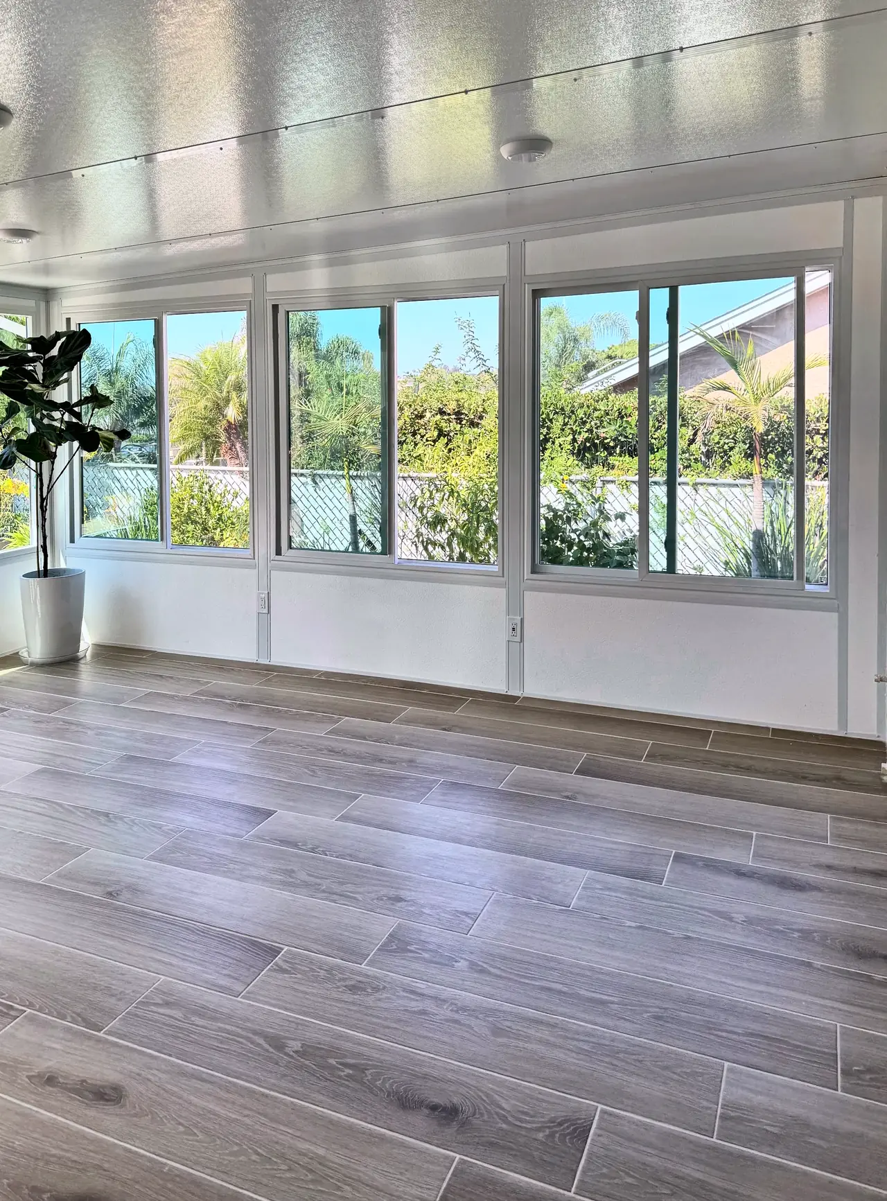 Sliding windows over a low white wall along the side of the room, with outlets in the wall, ceiling lights and a wood-look tile floor