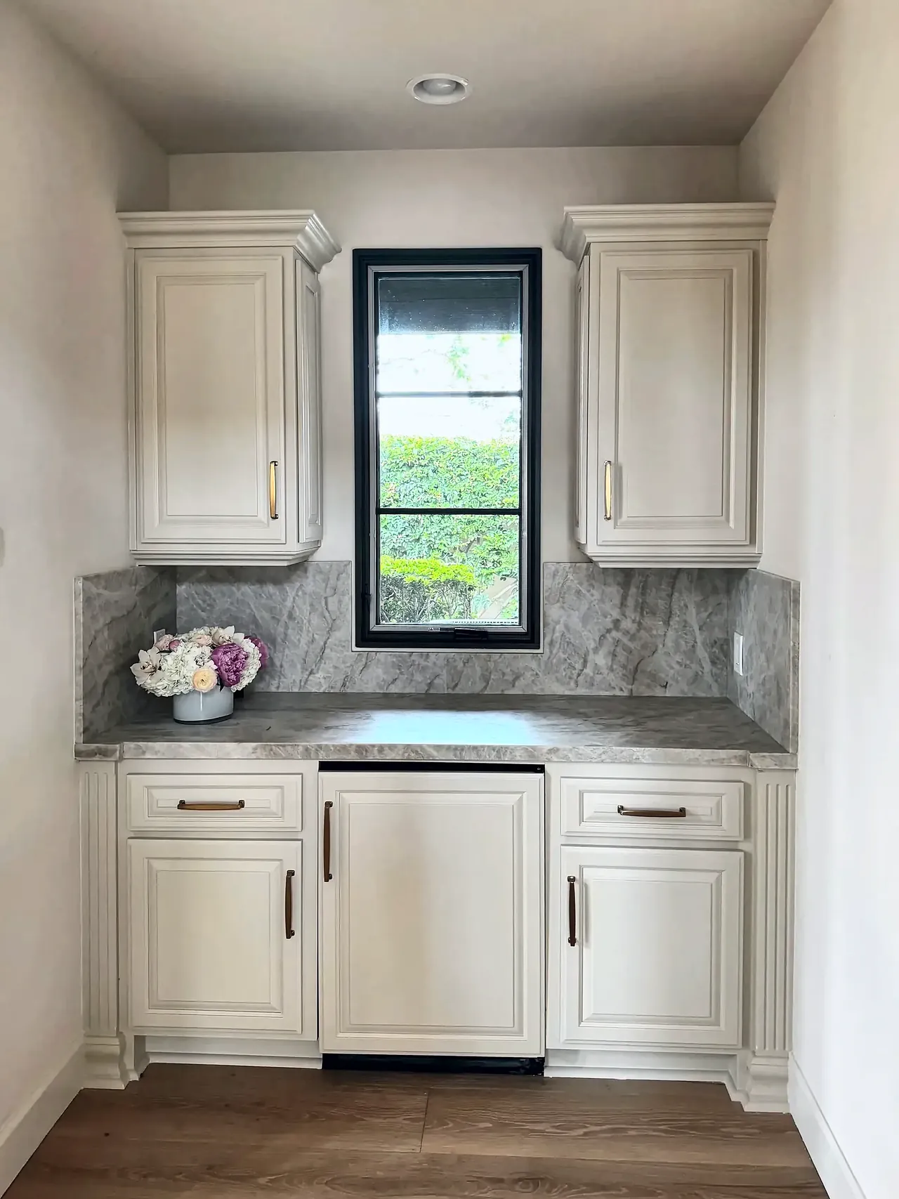Wet bar after, with cream refinished cabinets, brass pulls and a full-height stone backsplash