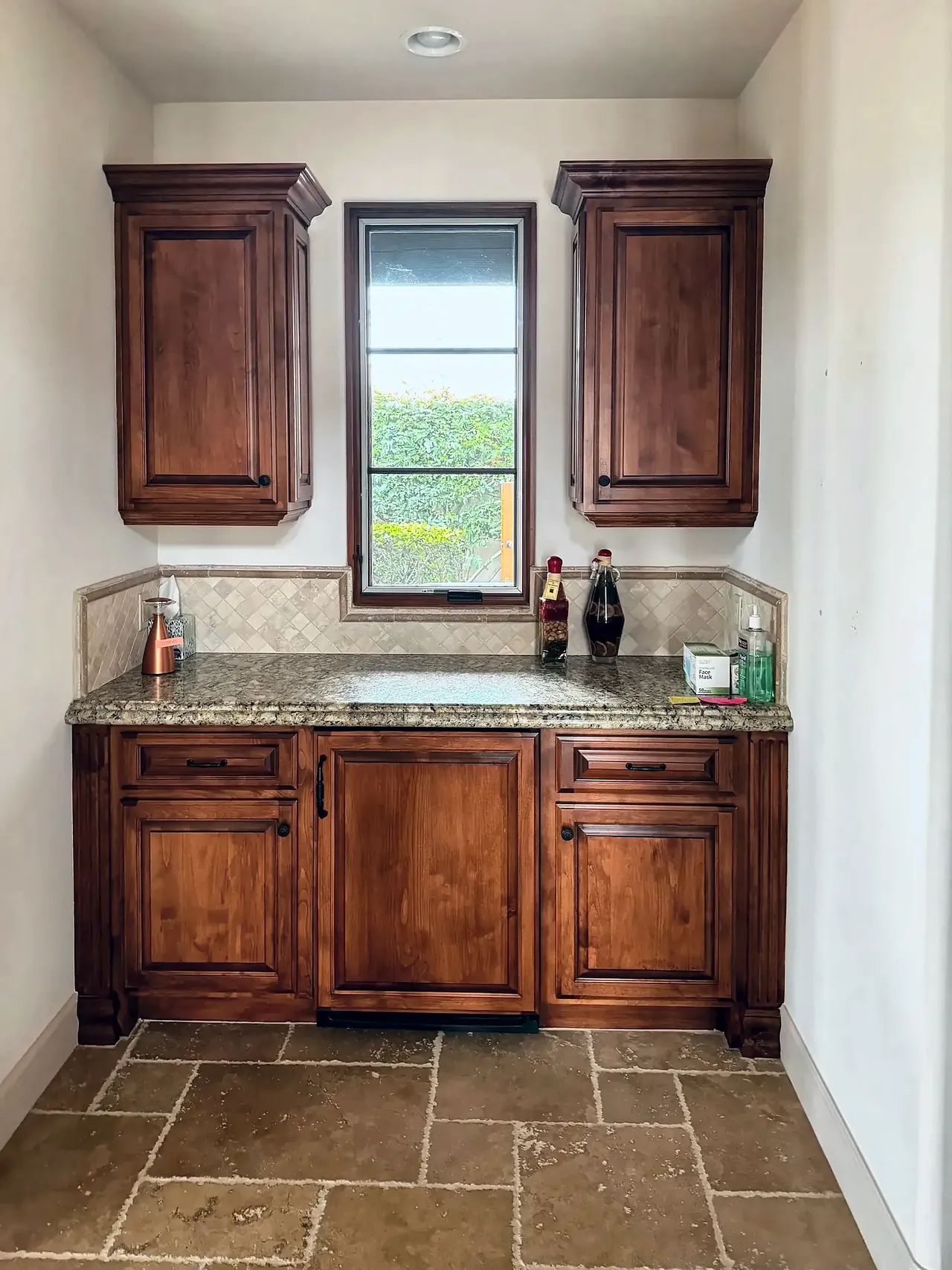 Wet bar before, with orange-stained cabinets, granite and a travertine backsplash